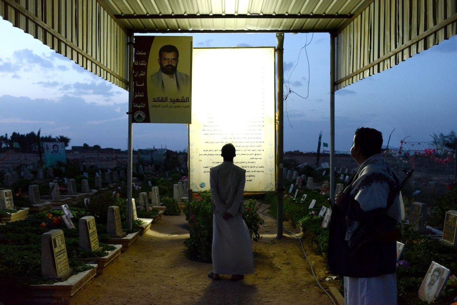 Two Yemeni men visit a graveyard and memorial of war martyrs.