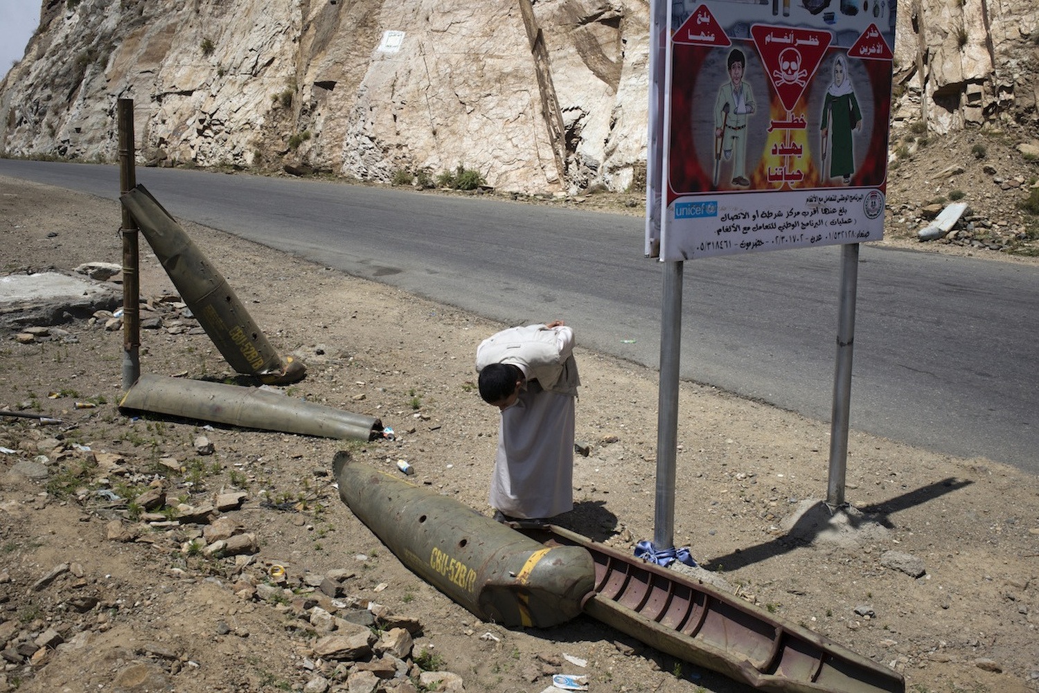 A Houthi supporter looks at shells left from the last war in Sa'ada, in 20TK. Missiles bearing the name of the United States armed forces still lay on the mountain slopes.