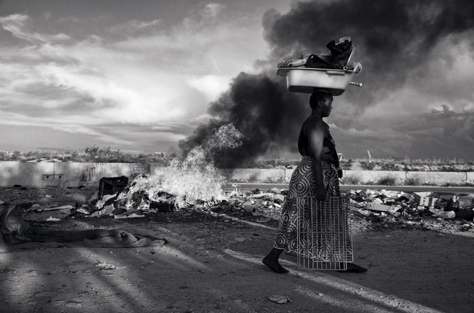 A street vendor passing a heap of burning trash, Diepsloot township, Johannesburg. Photograph by James Oatway for Harper’s Magazine © The artist