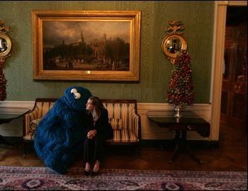 [Photo: A large blue creature, presumably a person in costume, sits next to a woman in the White House Green Room.]