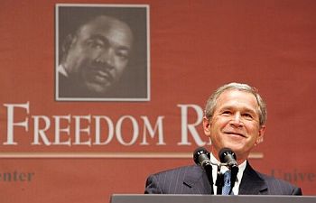 A photo of a smiling George W. Bush standing at a podium, with a photo of Martin Luther King, Jr. behind him.